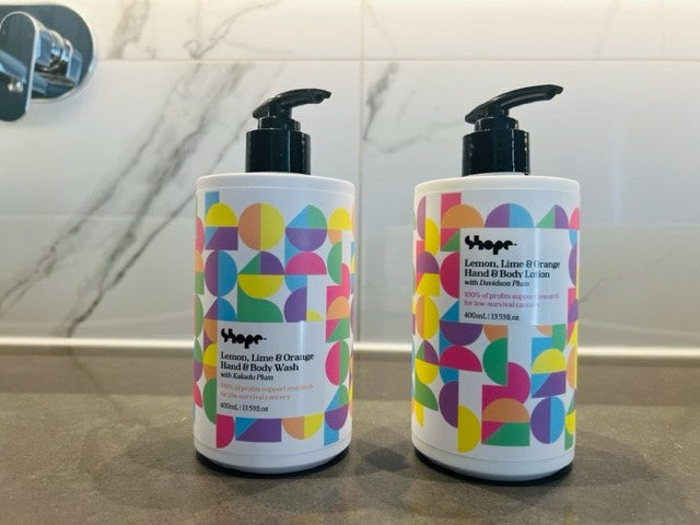 Boxed SHOPE lemon lime and orange hand and body wash and hand and body lotion, sitting on luxe bathroom countertop with silver tap and marble wall in background.
